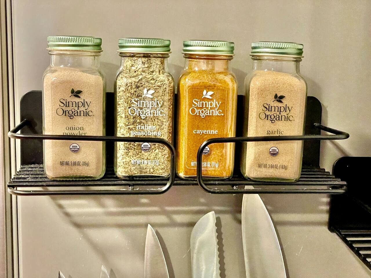 Quatre pots d’épices de la marque Simply Organic, rangés sur une étagère dans la cuisine.