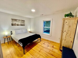 A bedroom with a bed, bedside tables, a window, and a wooden wardrobe. - Peaceful Cottage with Hot-tub in Fleetwood, North Carolina (Fleetwood)