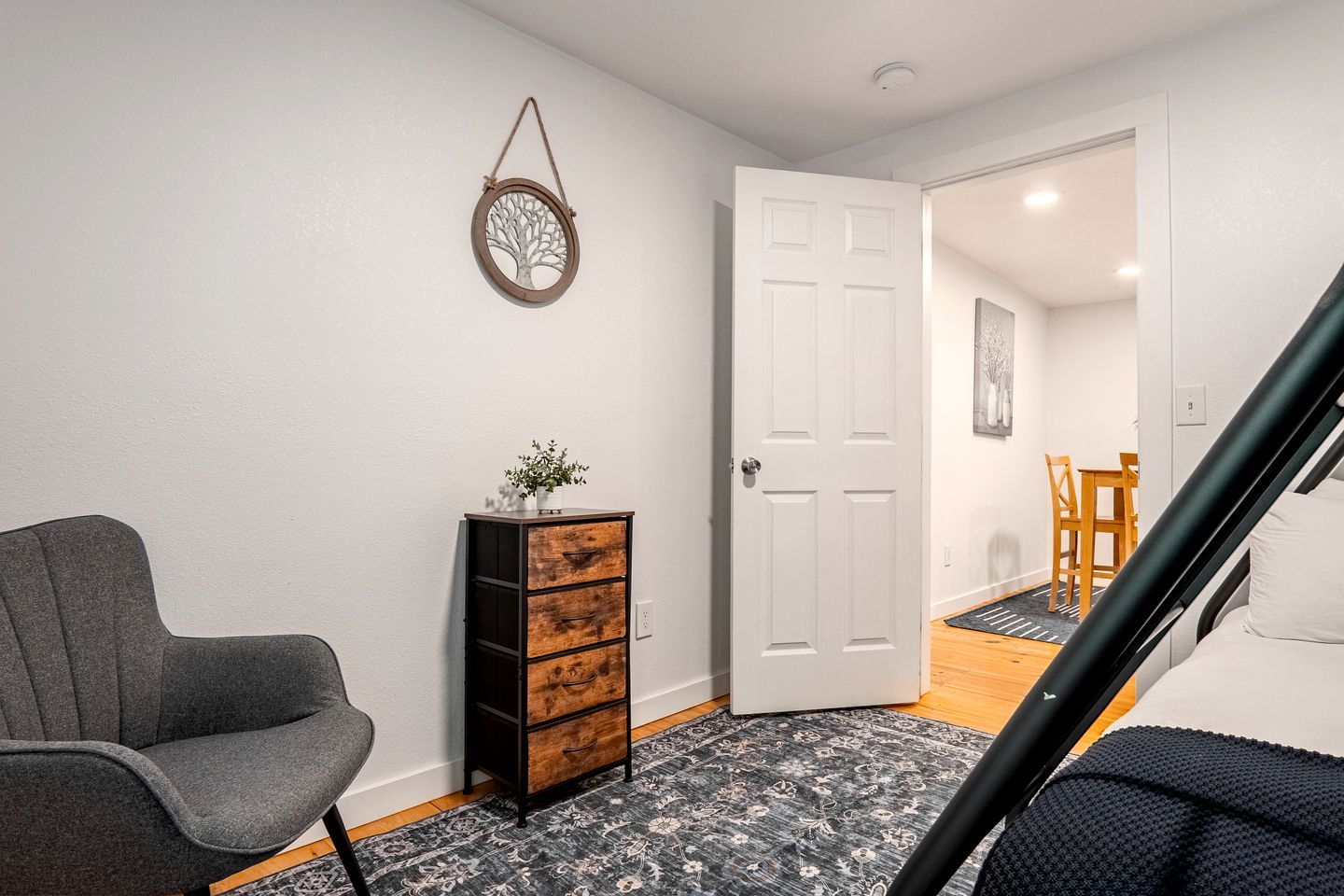 A room with a grey armchair, a wooden cabinet with drawers, a door, and a patterned rug.
