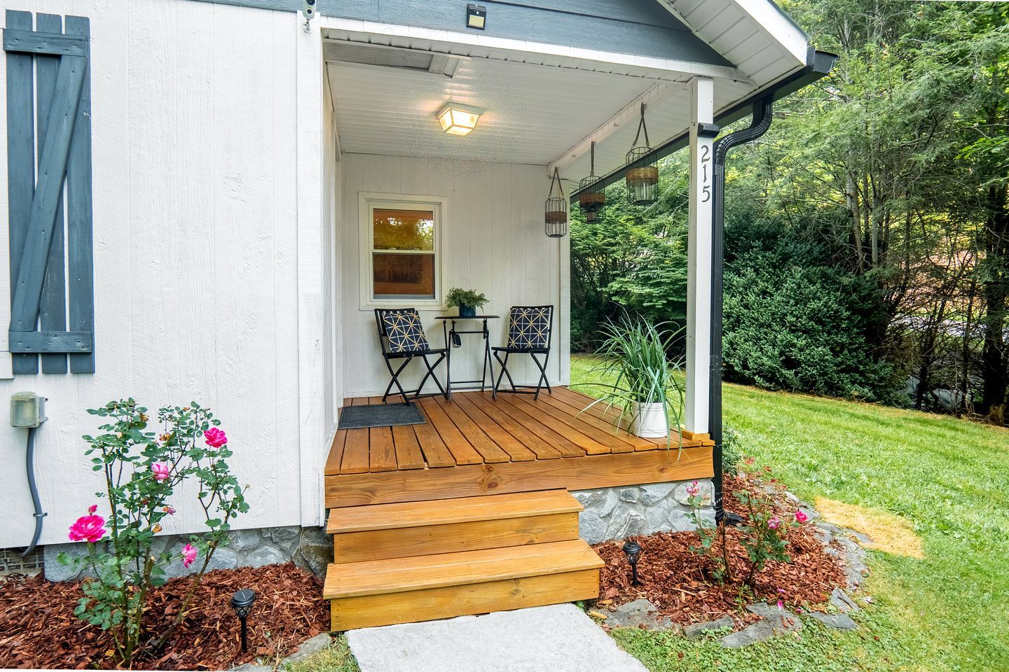 A house with a wooden porch, two chairs, a small table, and a potted plant.
