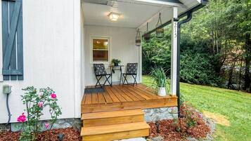 A house with a wooden porch, two chairs, a small table, and a potted plant.