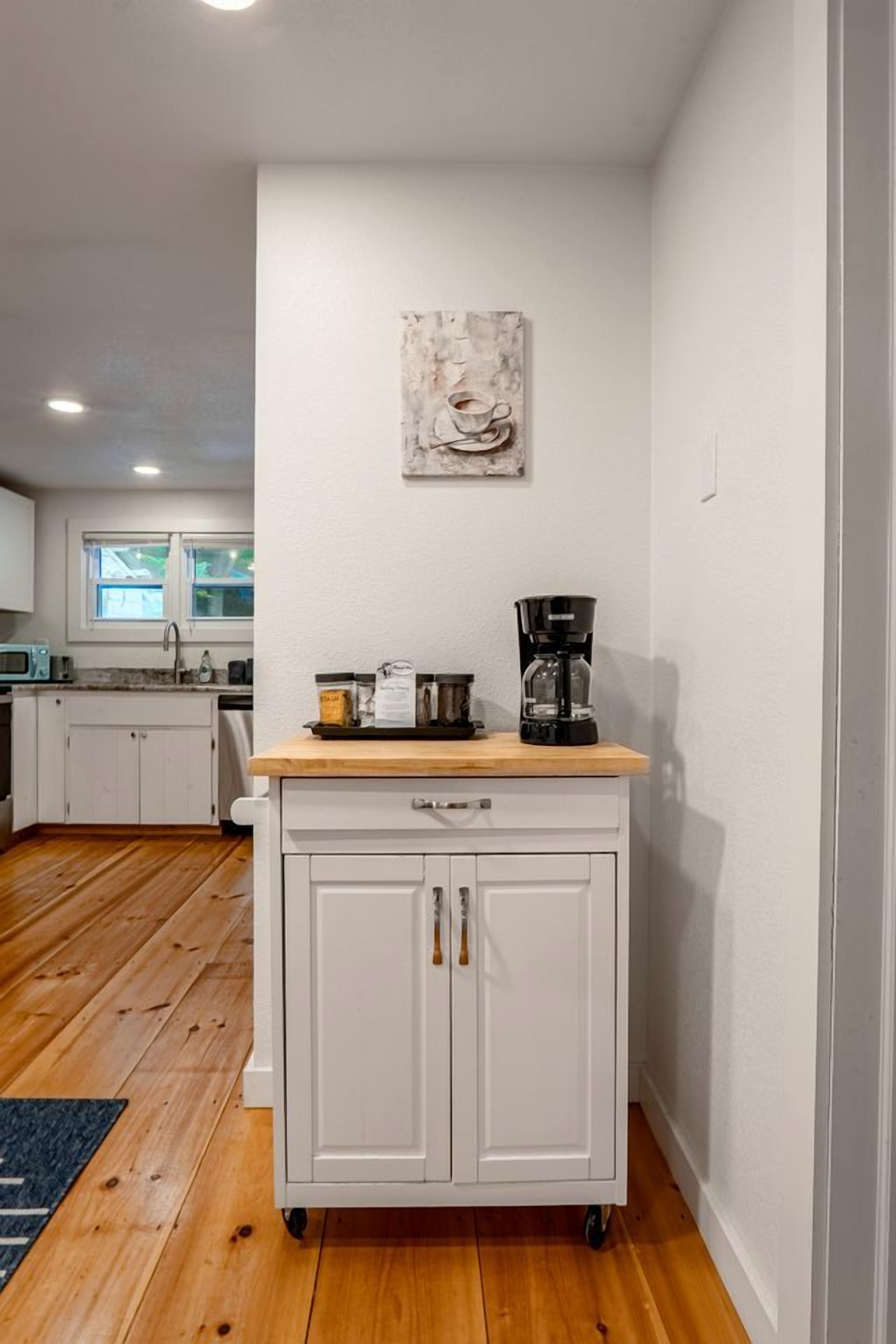 A kitchen with a white cabinet, a coffee maker, and a rustic artwork on the wall.