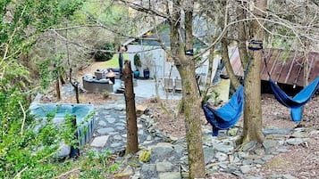A rustic outdoor setting with a hammock, a shed, and a garden area with rocks and plants.