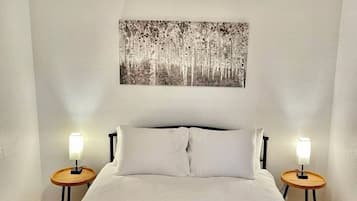 A bedroom with a bed, two bedside tables with lamps, a ceiling light, and a wall-mounted painting.