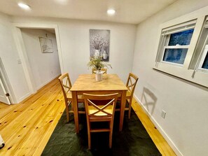 A dining area with a wooden table and chairs, a vase with flowers, and a painting on the wall.