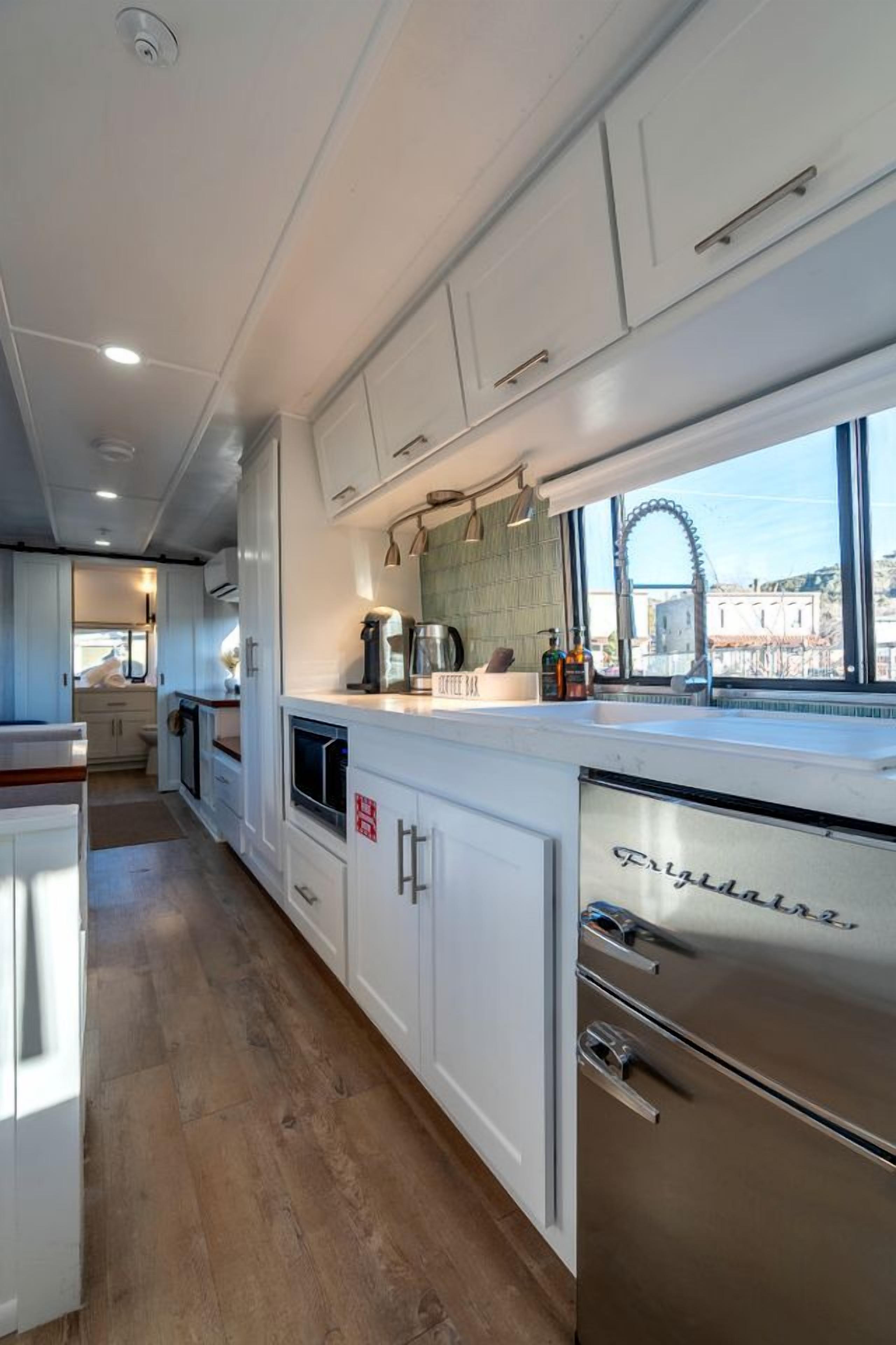 A modern kitchen with white cabinetry, a stainless steel refrigerator, and a window overlooking a cityscape.