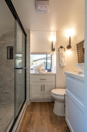 Ein Badezimmer mit Duschkabine aus Glas, Toilette und Waschbecken mit Spiegel.