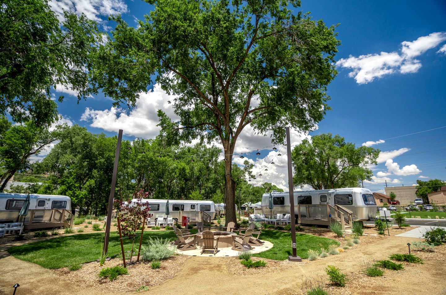 Un terrain de camping équipé d’emplacements pour camping-cars, d’un foyer pour faire des feux de camp et bordé d’arbres.
