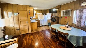 Una cocina compacta con paredes de madera, un comedor con una mesa y un televisor montado en la pared.