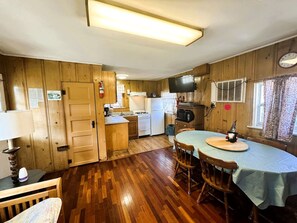 Une cuisine compacte aux murs en bois, un coin repas avec une table et un téléviseur fixé au mur.