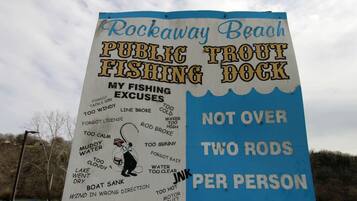 Bordje voor de Rockaway Beach Public Trout Fishing Dock met een lijst van excuses voor het vissen en een regel: maximaal twee hengels per persoon.