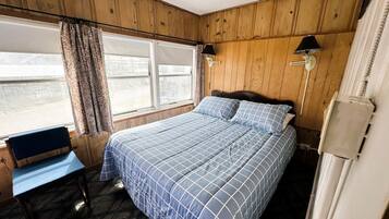 A bedroom with a bed, a chair, a window, and a lamp.