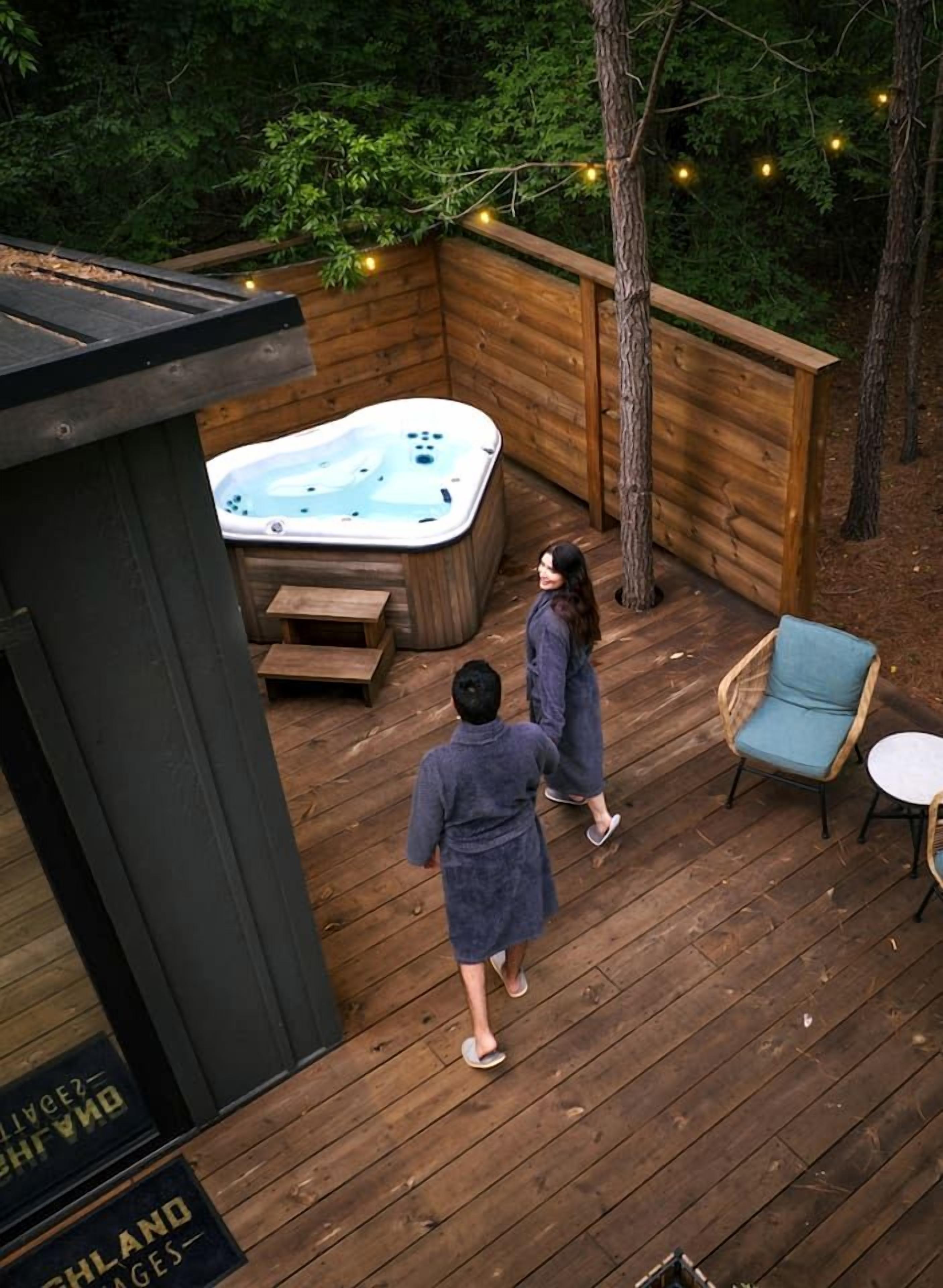 Een houten terras met een jacuzzi, zithoek en een houten omheining.