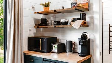 Une cuisine équipée d’un four à micro-ondes, d’un grille-pain, d’une bouilloire et d’une machine à café, le tout posé sur le plan de travail, avec des étagères au-dessus pour ranger divers objets.