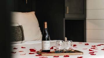 A bed with a white bedspread, a bottle of wine, two glasses, and a tray with rose petals.