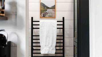 A towel hanging on a black towel rack in a bathroom with a picture of a landscape on the wall.