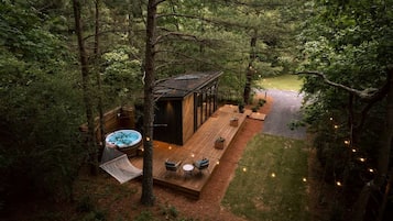 A wooden deck with outdoor seating, a hot tub, and a small building, surrounded by dense forest.