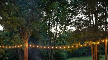 An outdoor seating area with chairs and a fire pit, surrounded by trees and string lights.