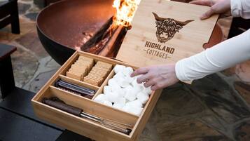 A wooden box with a logo and text, held by a person, next to a fire pit with logs.