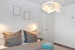 Ett sovrum med en säng, två kuddar, ett sängbord, en lampa och en väggmonterad lamparmatur.