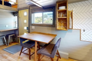 A compact kitchen with a wooden table and chairs, a window with a view, and a herringbone-patterned wall.