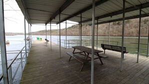 Una terraza de madera techada con una mesa de picnic y bancos, con vista a un cuerpo de agua.