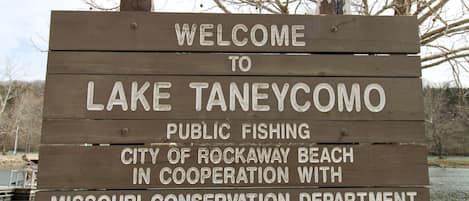 Señal de madera que da la bienvenida al lago Taneycomo, indicando pesca pública y colaboración con el Departamento de Conservación de Missouri.