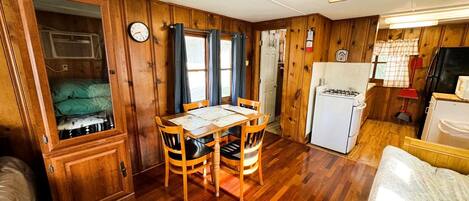 A compact kitchen with wooden cabinets, a dining table with chairs, a refrigerator, and a microwave.