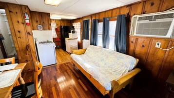 A compact RV interior with a bed, kitchenette, and wooden walls.