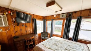 Un interior de cabaña con cama, escritorio, silla, televisor y ventanas.