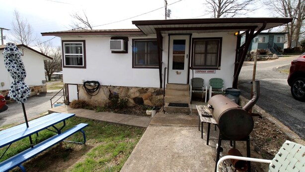 Un pequeño edificio con una puerta que dice 'ORPHAN ANNIE', una parrilla, una mesa de picnic y una silla afuera.