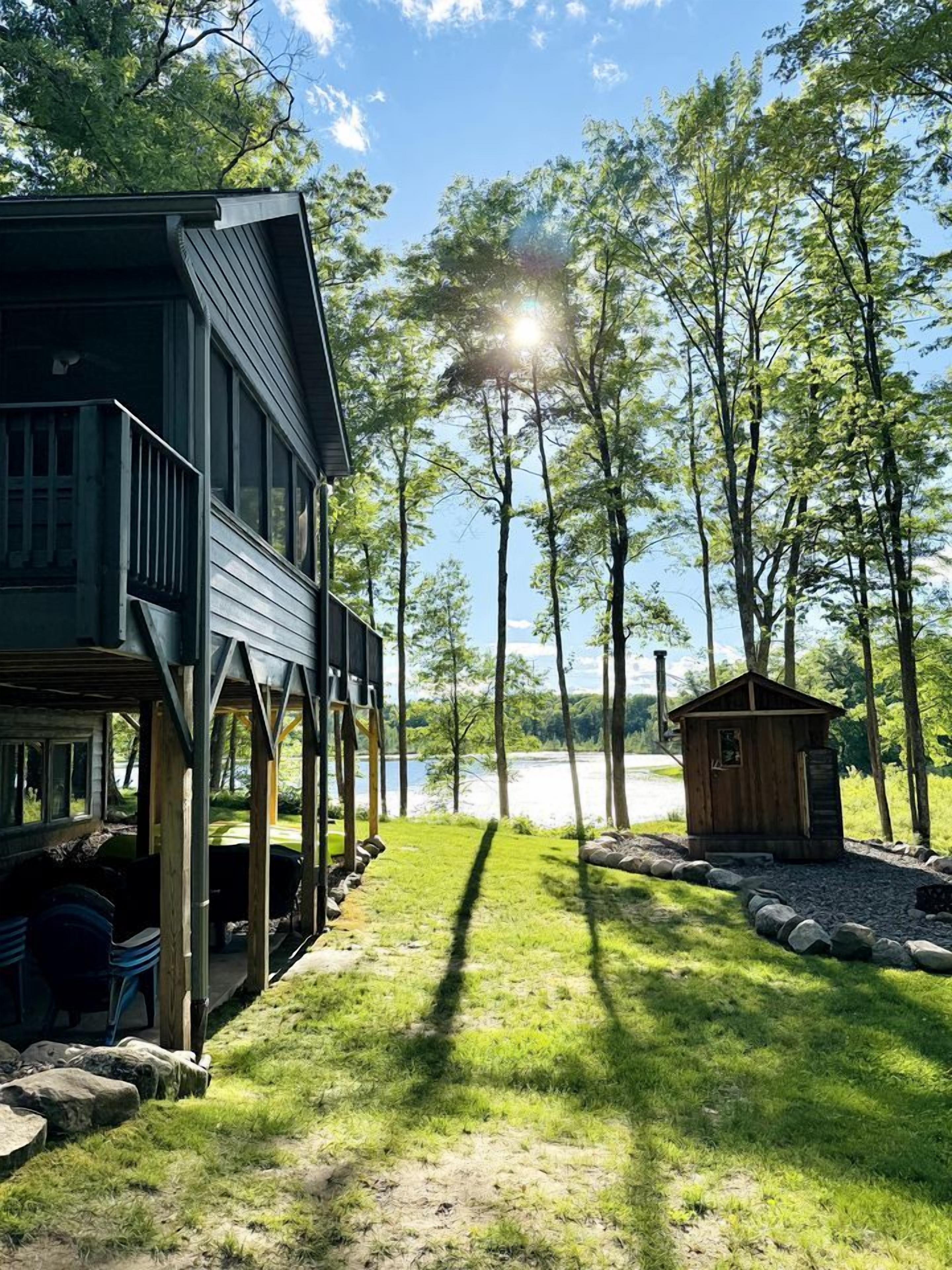A cabin with a deck, a small shed, and a grassy area leading to a body of water.