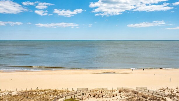 A beach with a sandy shore, a clear sky, and a few people walking. - Direct Oceanfront Two Bedroom Condo with Pool (Ocean City)