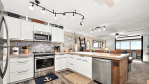 A modern kitchen with white cabinets, stainless steel appliances, a wooden island, and a dining area with a view. - Direct Oceanfront Two Bedroom Condo with Pool (Ocean City)