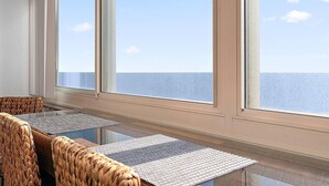 A room with a view of the sea, wicker furniture, and a glass table. - Direct Oceanfront Two Bedroom Condo with Pool (Ocean City)
