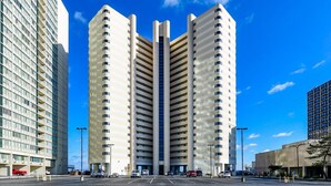 A modern high-rise building with a central atrium, surrounded by a parking lot and other buildings. - Direct Oceanfront Two Bedroom Condo with Pool (Ocean City)