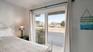A bedroom with a bed, a nightstand, a lamp, a window with a view of a beach, and a sign indicating no swimming.