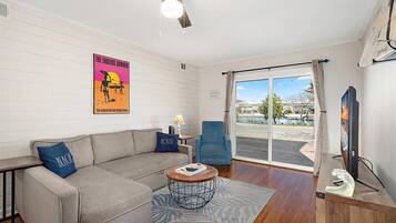 A living room with a sofa, armchair, coffee table, and a poster on the wall.