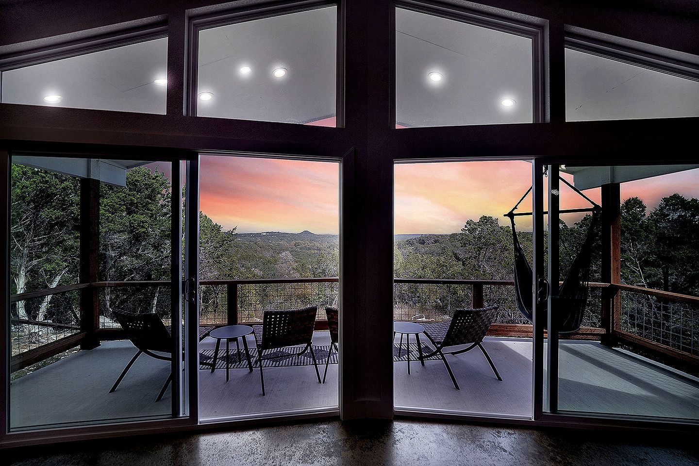 A room with large windows, a balcony with chairs, and a view of the landscape.