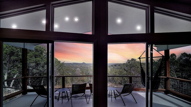 Ein Zimmer mit großen Fenstern, einem Balkon mit Sitzgelegenheiten und Blick auf die Landschaft.