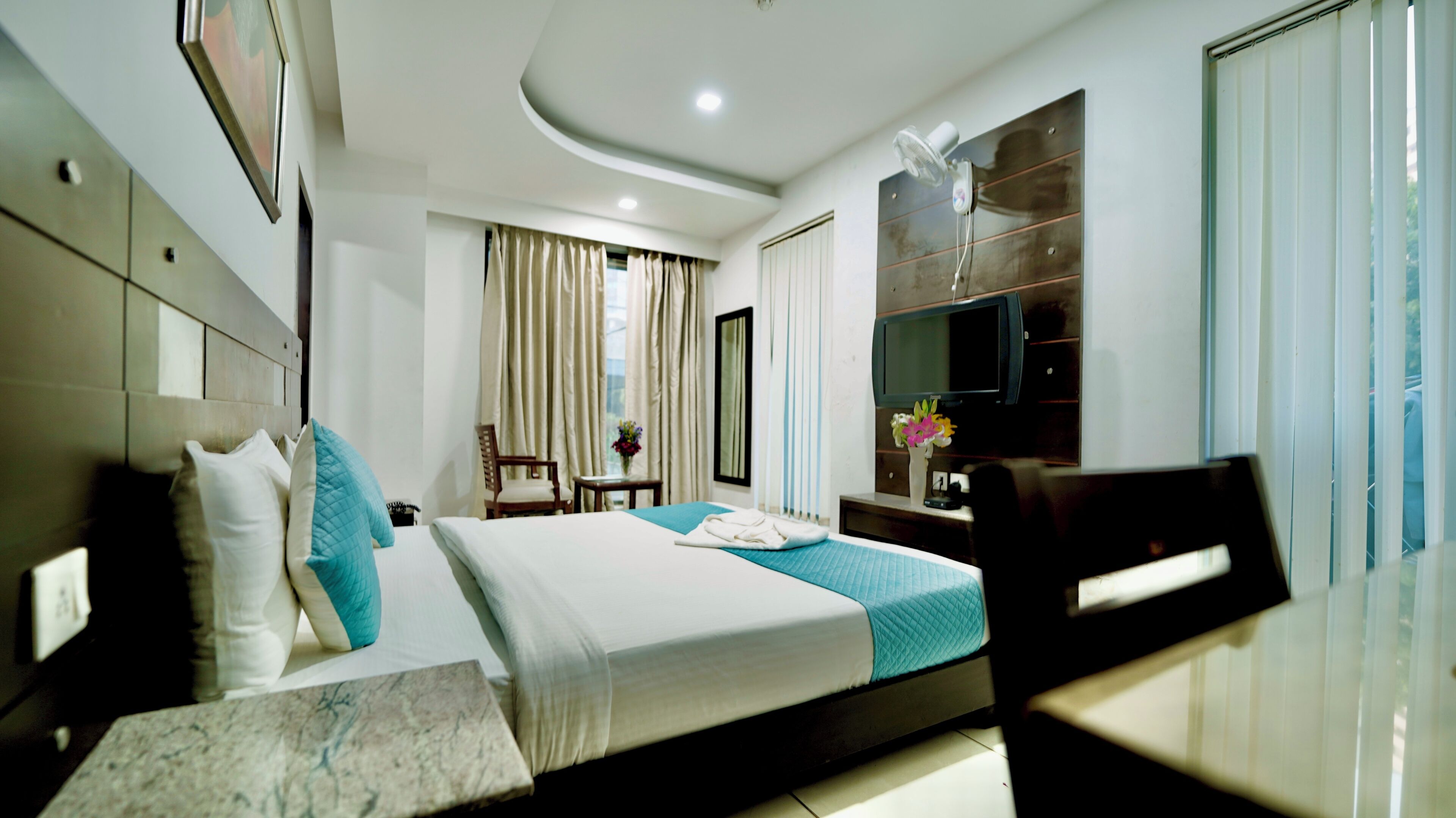 A hotel room with a bed, a desk, a chair, a TV, and a window with curtains.