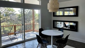 Una habitación moderna con una mesa redonda, sillas, una lámpara colgante y ventanas amplias.