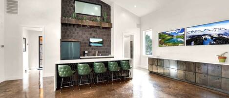 Une cuisine moderne dotée d’un four encastré, d’une grande fenêtre et d’un coin bar avec des tabourets verts.