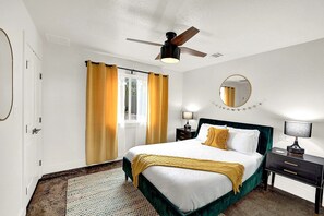 A hotel room with a bed, a ceiling fan, a window with curtains, a bedside table with a lamp, and a mirror on the wall. - Stunning Three Cabins Great for Groups in Wimberley, Texas (Wimberley)