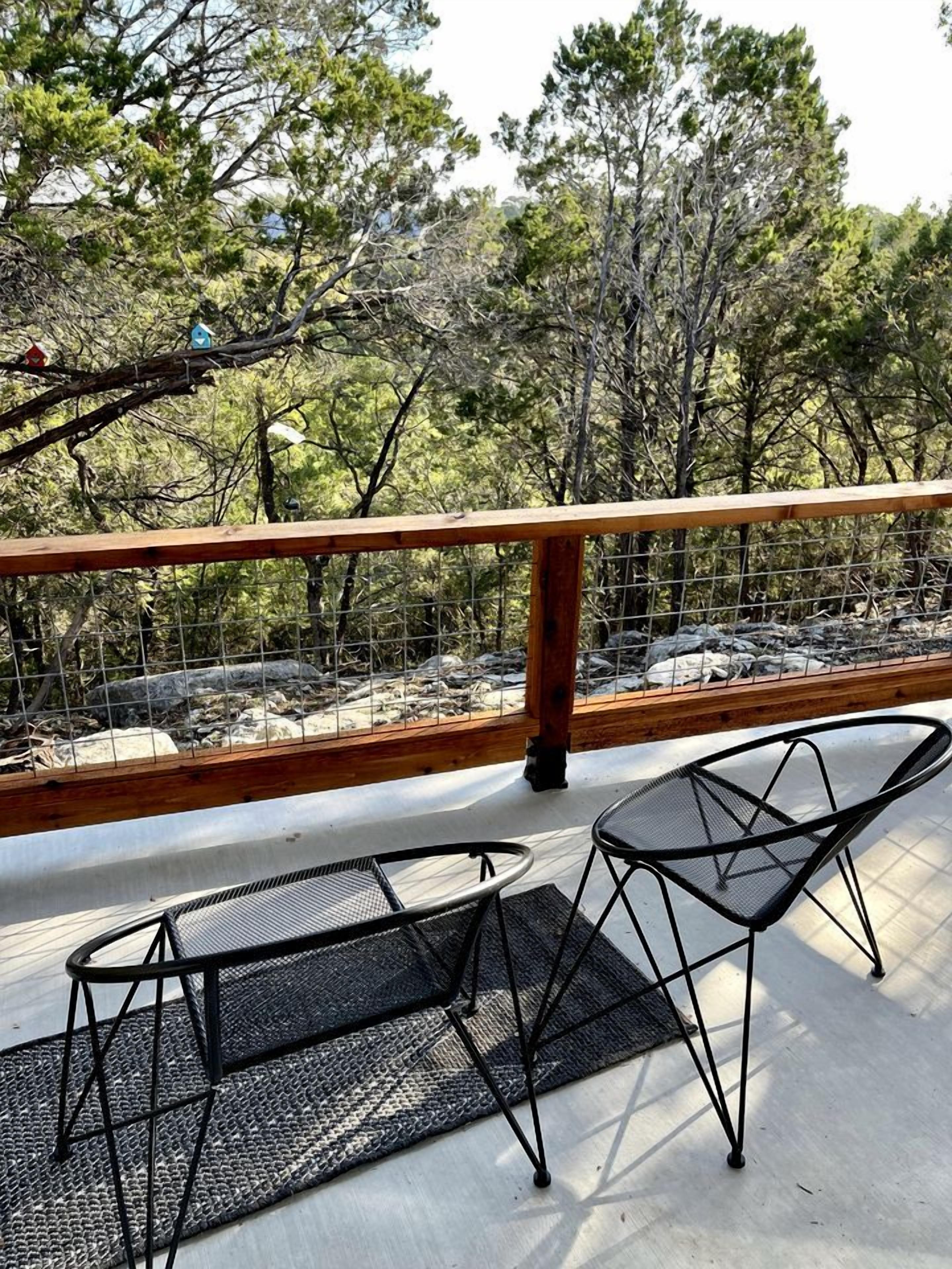 A balcony with a wooden railing, two black mesh chairs, and a view of trees and rocks.
