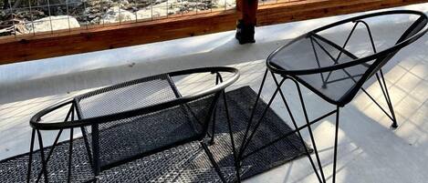 A balcony with a wooden railing, two black mesh chairs, and a view of trees and rocks.