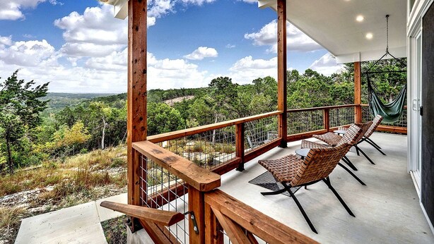 Une terrasse en bois, meublée de meubles en osier, avec un hamac et une vue sur un paysage boisé.