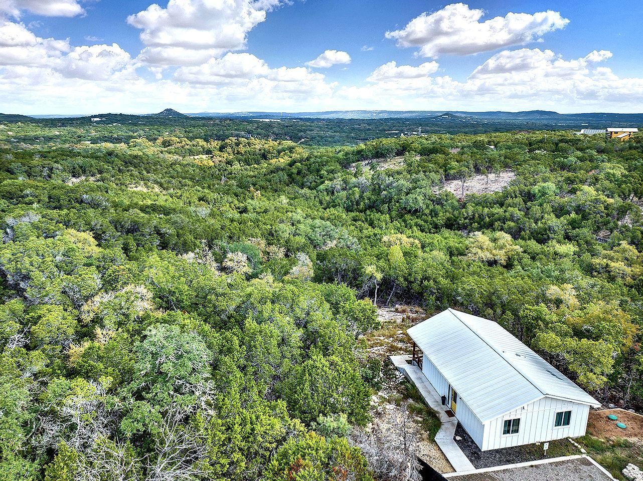 A white building with a sloped roof surrounded by dense green forest.