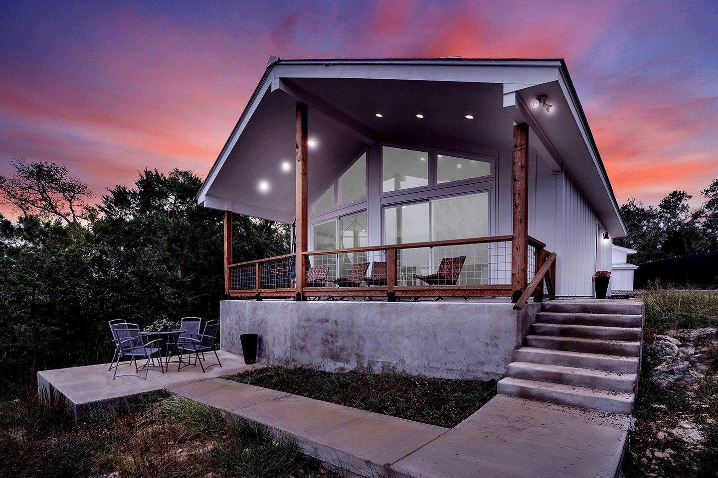 A modern house with a large glass window, a concrete deck, and a wooden staircase.