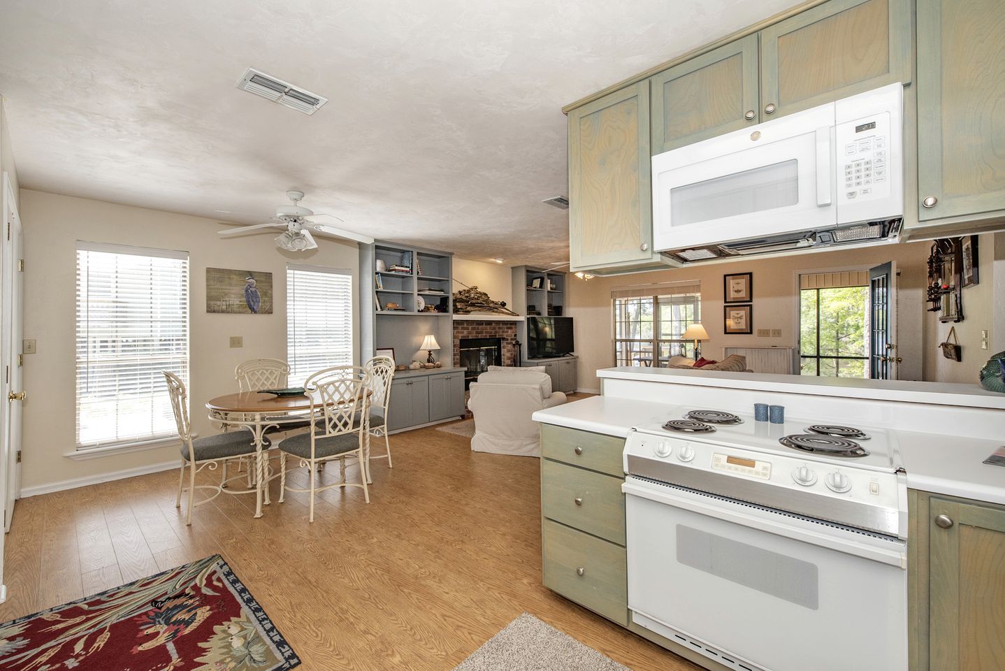Une cuisine équipée d’une cuisinière, d’un four à micro-ondes et de placards. On y trouve une table à manger avec des chaises et un ventilateur de plafond.